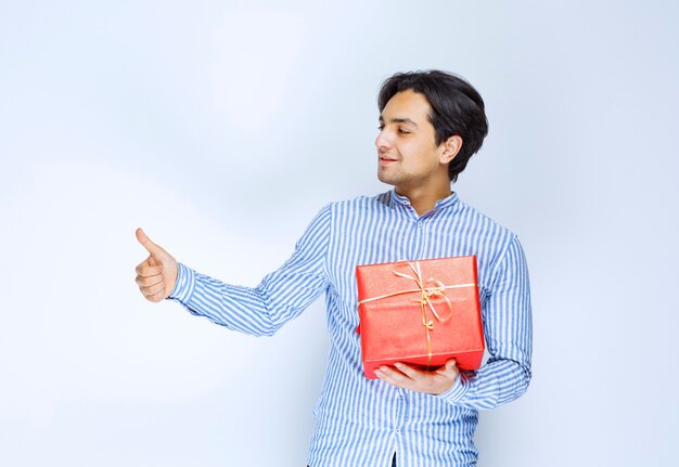 Hombre con una caja de regalo roja mostrando el pulgar hacia arriba. Foto de alta calidad