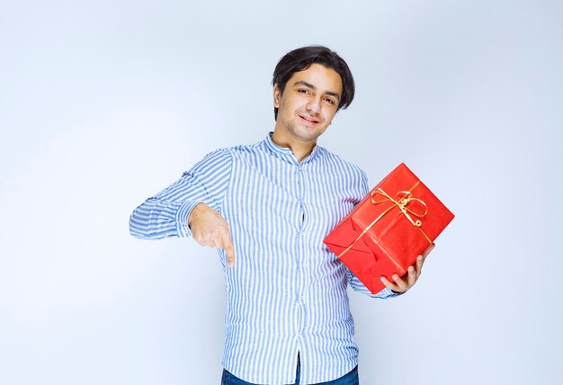 Hombre con una caja de regalo roja notando a una persona adelante y llamándolo para presentar el regalo. Foto de alta calidad