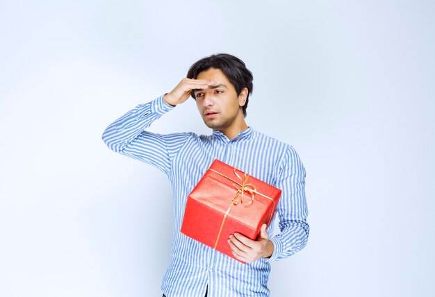 El hombre con una caja de regalo roja parece cansado y aburrido. Foto de alta calidad