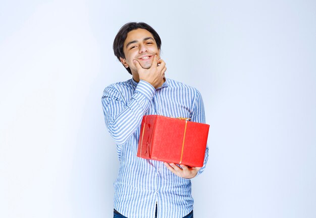 Hombre con una caja de regalo roja pidiendo una sonrisa. Foto de alta calidad