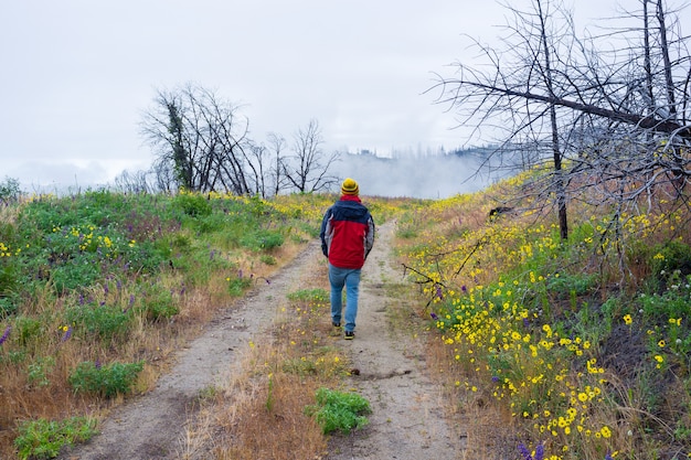 Hombre en una cálida chaqueta caminando por un camino estrecho en un hermoso campo