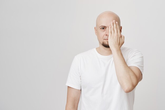 Hombre calvo de aspecto serio cubre la mitad de la cara con la mano