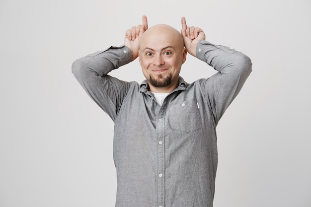 Hombre Calvo gracioso tonto mostrando cuernos detrás de la cabeza