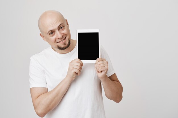 Hombre Calvo guapo mostrando la pantalla de la tableta digital, sonriendo complacido