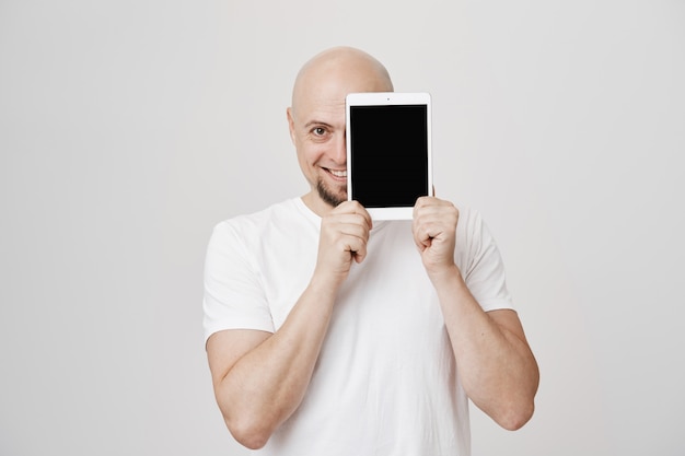Hombre Calvo guapo mostrando la pantalla de la tableta digital, sonriendo complacido