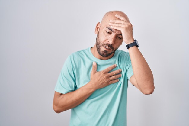 Hombre calvo de mediana edad parado sobre fondo blanco tocando la frente por enfermedad y fiebre, gripe y resfriado, enfermo de virus