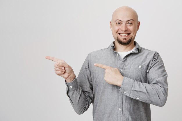 Hombre calvo sonriente complacido apuntando a la izquierda