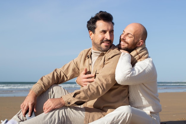 Hombre calvo sonriente sentado en la arena con su novio