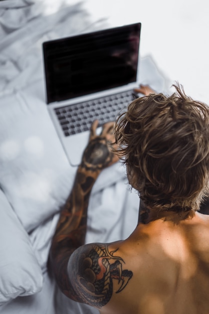 Foto gratuita un hombre en la cama trabajando en una computadora portátil, revisando el correo, viendo una película, escuchando música