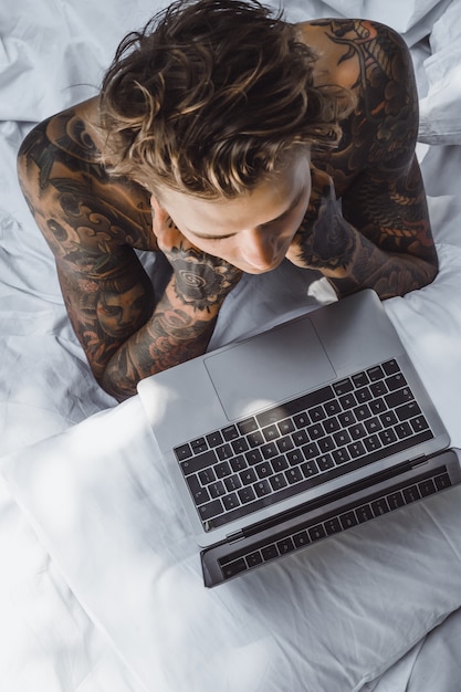 un hombre en la cama trabajando en una computadora portátil, revisando el correo, viendo una película, escuchando música