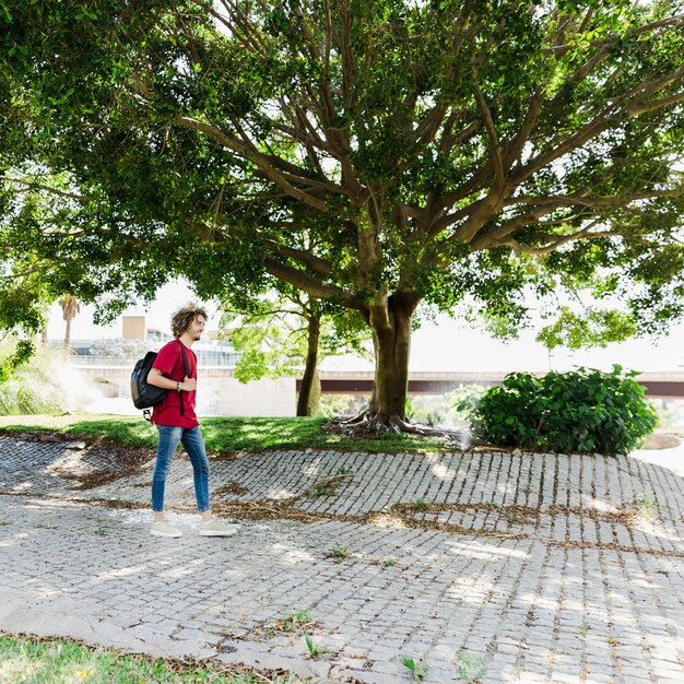 Hombre caminando con mochila cerca de un árbol