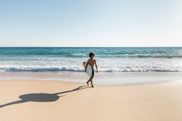 Hombre caminando en la playa con tabla de surf