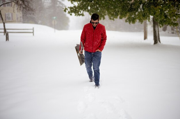 Hombre caminando sobre un campo cubierto de nieve mientras sostiene la pala de nieve