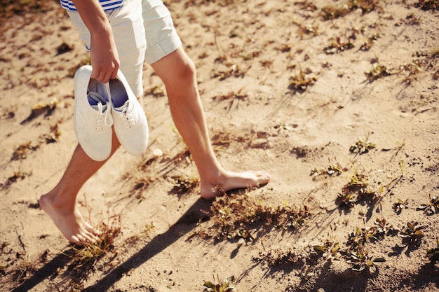 Hombre caminando con los zapatos en la mano en la playa