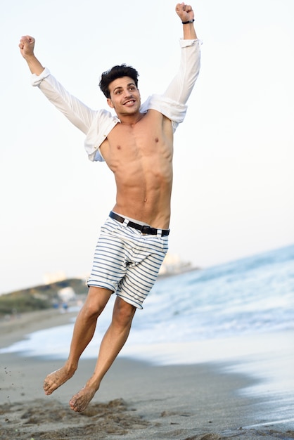 Hombre con la camisa abierta en la playa saltando