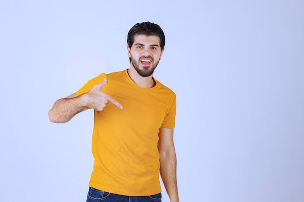 Hombre de camisa amarilla apuntando a sí mismo.