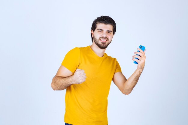 Hombre de camisa amarilla apuntando con su teléfono inteligente y disfrutándolo.