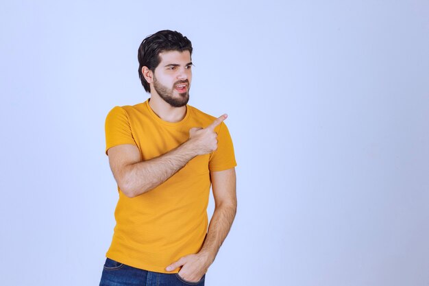 Hombre con camisa amarilla mostrando algo a la derecha.