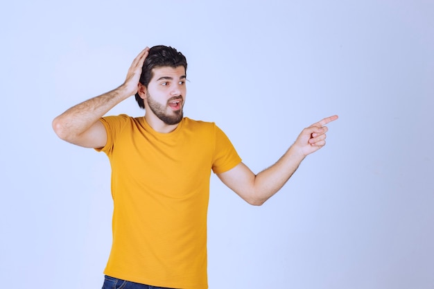 Hombre con camisa amarilla mostrando algo a la derecha.