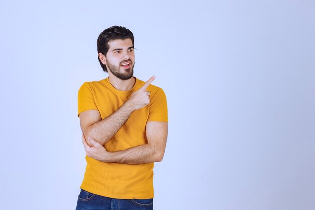 Hombre con camisa amarilla mostrando algo a la derecha.