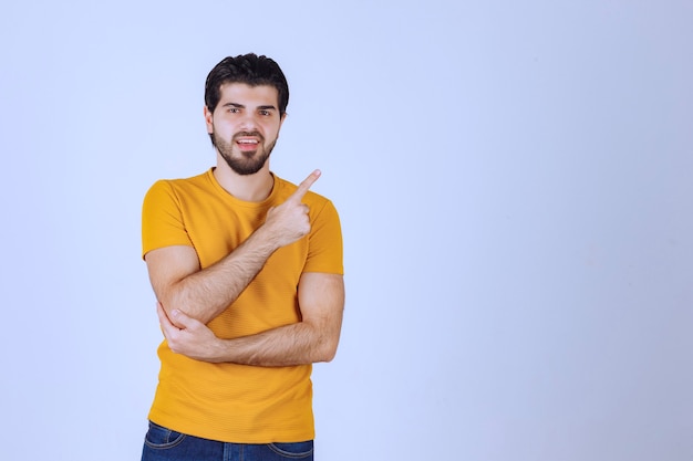 Hombre con camisa amarilla mostrando algo a la derecha.