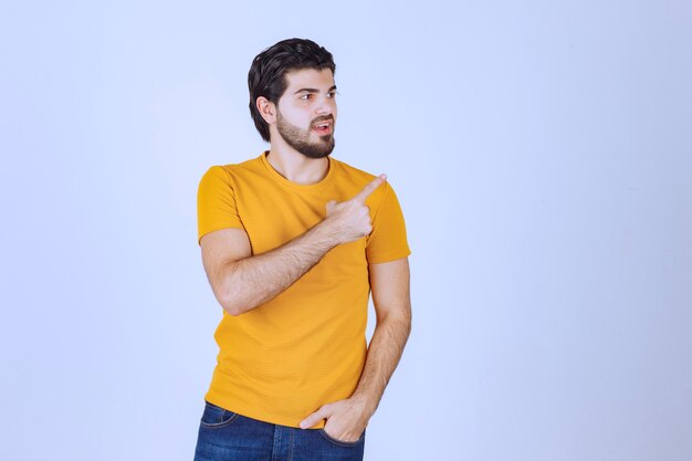 Hombre con camisa amarilla mostrando algo a la derecha.