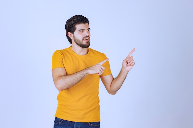 Hombre con camisa amarilla mostrando algo a la derecha.