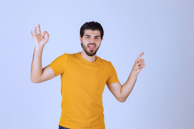 Hombre con camisa amarilla mostrando algo a la derecha.