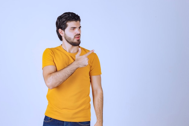 Hombre con camisa amarilla mostrando algo a la derecha.