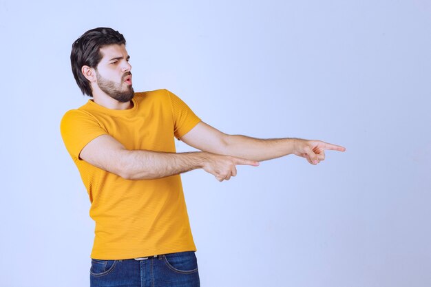 Hombre con camisa amarilla mostrando algo a la derecha.