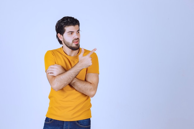 Hombre con camisa amarilla mostrando algo a la derecha.