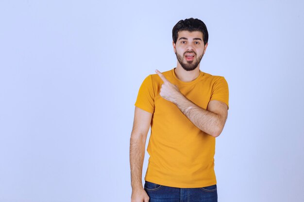 Hombre con camisa amarilla mostrando algo a la izquierda.