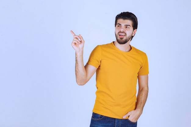 Hombre con camisa amarilla mostrando algo a la izquierda.