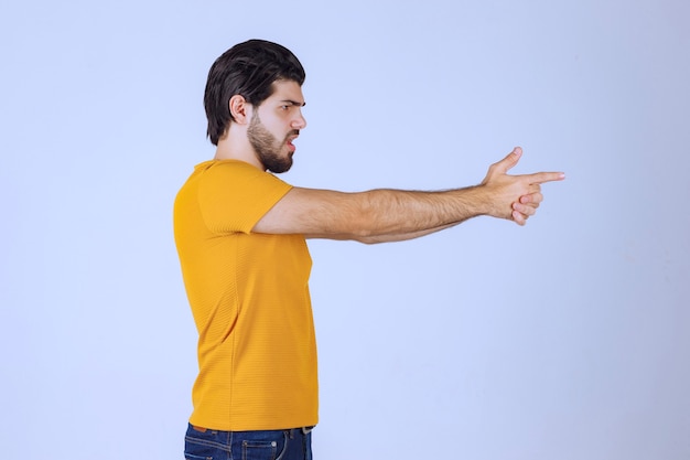 Foto gratuita hombre de camisa amarilla mostrando signo de pistola en la mano