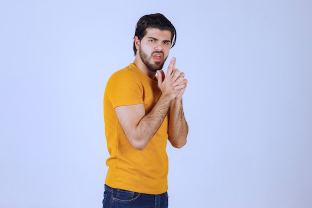 Hombre de camisa amarilla mostrando signo de pistola en la mano