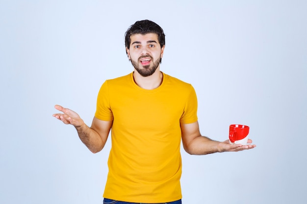 Hombre de camisa amarilla sosteniendo una taza roja y pensando.