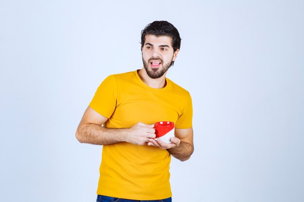 Hombre de camisa amarilla sosteniendo una taza roja y pensando.