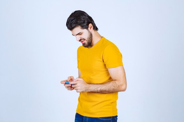 Hombre de camisa amarilla sosteniendo un teléfono inteligente azul.
