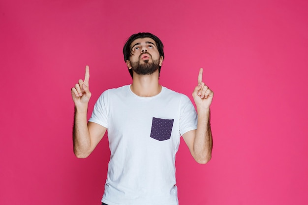 Hombre con camisa blanca apuntando a algo arriba.