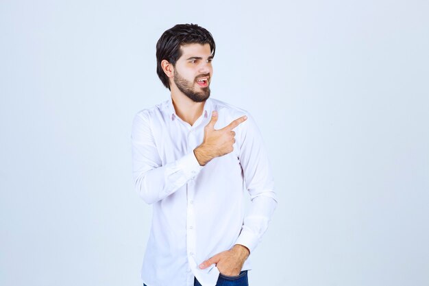 Hombre con camisa blanca apuntando a algo a la derecha.