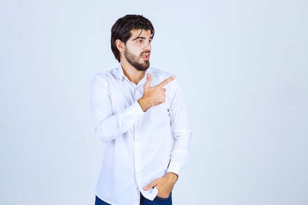 Hombre con camisa blanca apuntando a algo a la derecha.