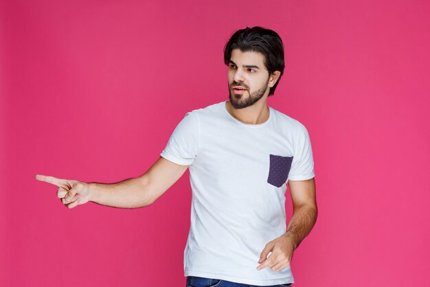 Hombre con camisa blanca apuntando a algo a la izquierda.