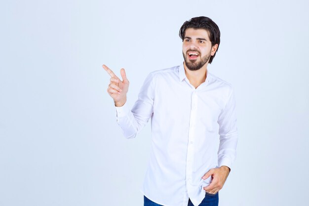 Hombre con camisa blanca apuntando en algún lugar de la izquierda con cara de emociones.