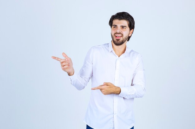 Hombre con camisa blanca apuntando en algún lugar de la izquierda con cara de emociones.