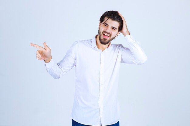 Hombre con camisa blanca apuntando en algún lugar de la izquierda con cara de emociones.