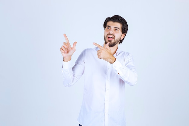 Hombre con camisa blanca apuntando en algún lugar de la izquierda con cara de emociones.