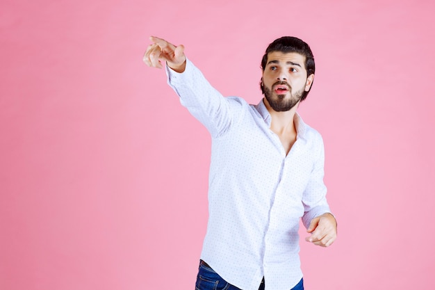 Foto gratuita hombre con camisa blanca apuntando hacia el lado izquierdo.