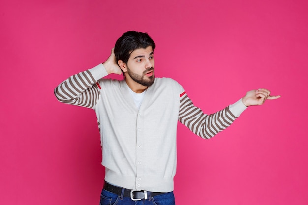 Foto gratuita hombre con camisa blanca apuntando y presentando algo en el lado derecho.