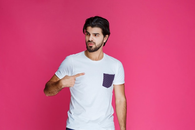 Hombre con camisa blanca apuntando a sí mismo.