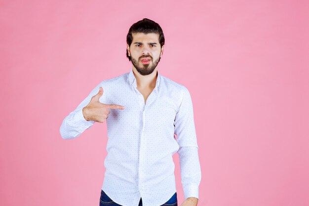 Hombre con camisa blanca apuntando a sí mismo.